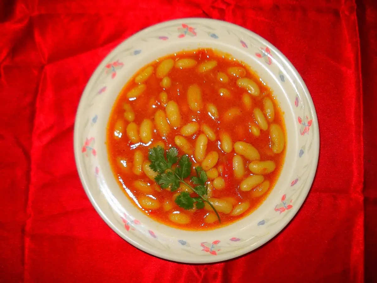 Plato de alubias blancas en salsa de tomate con perejil sobre un mantel rojo