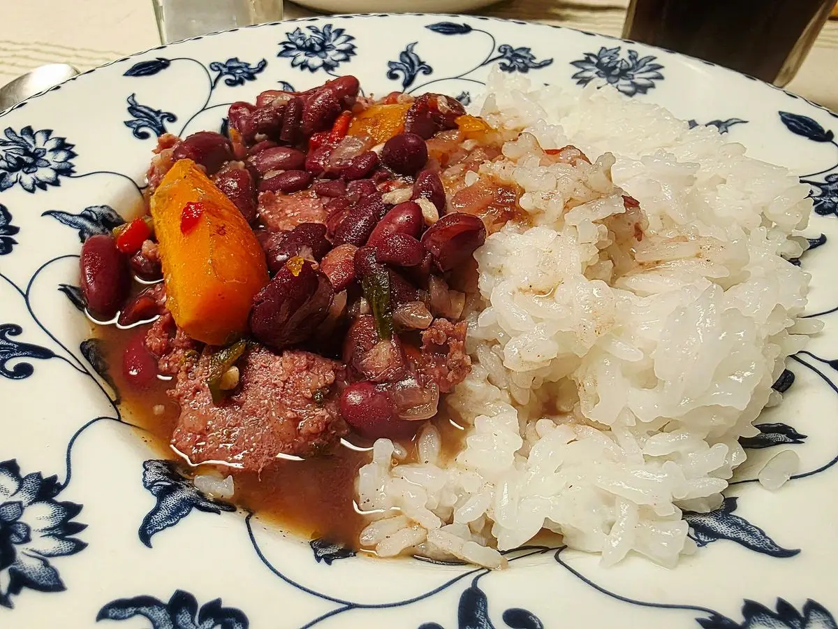 Plato de alubias guisadas con carne, zanahoria y arroz blanco sobre plato de porcelana azul