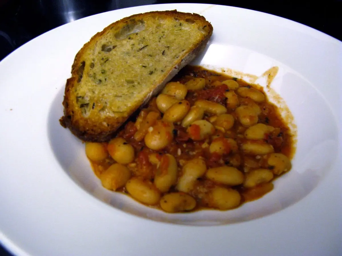 Alubias blancas en salsa de tomate con una rebanada de pan tostado en un plato hondo blanco