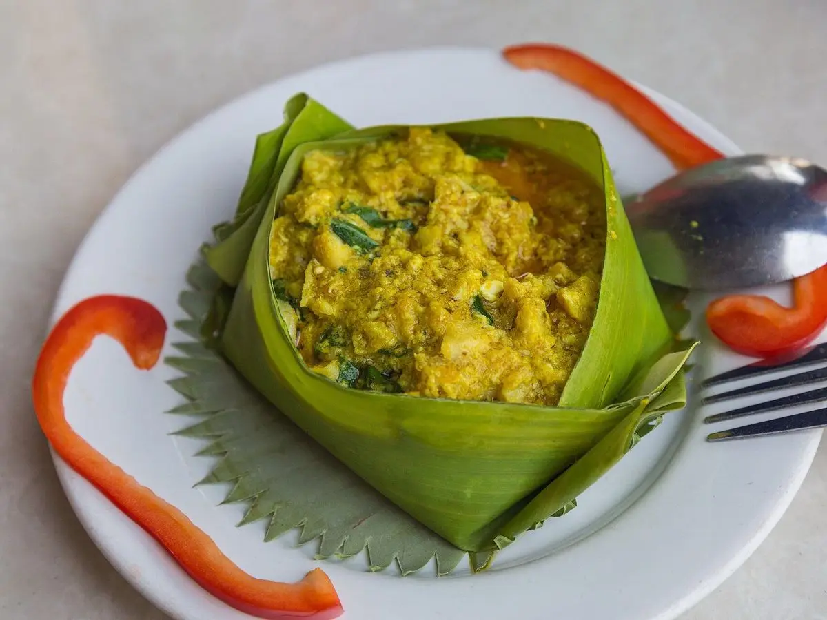 Pescado al vapor en crema de coco amarilla servido en un cesto de hoja de plátano
