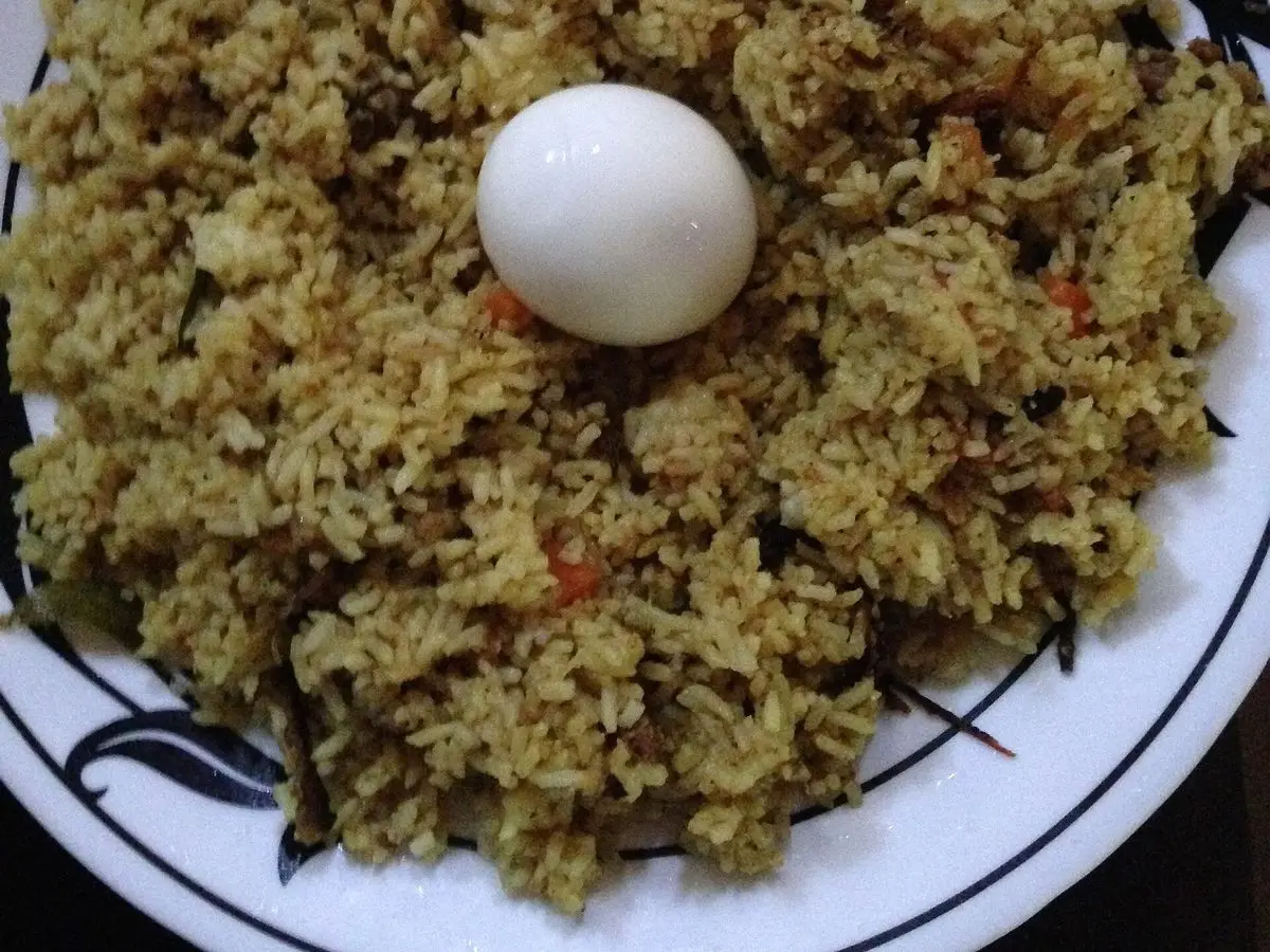 Biryani de arroz especiado con un huevo cocido entero encima en un plato con borde decorado