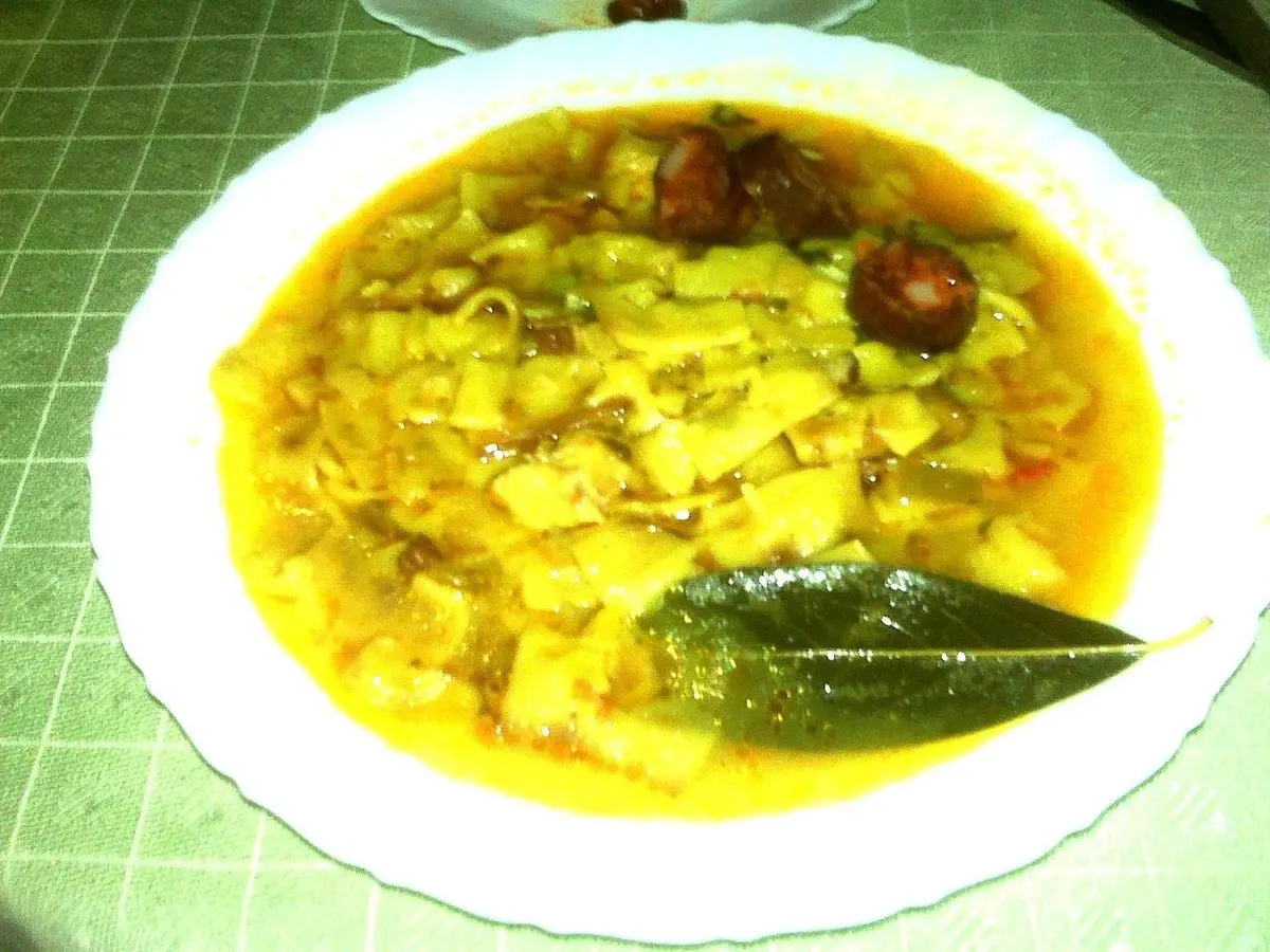 Plato hondo de andrajos, guiso de láminas de pasta en caldo amarillo con una hoja de laurel