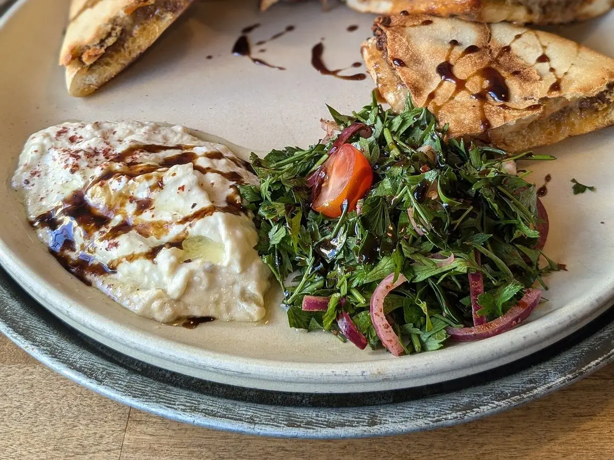 Pitas rellenas tostadas y cortadas en un plato blanco junto a una ensalada de hojas verdes y tomate