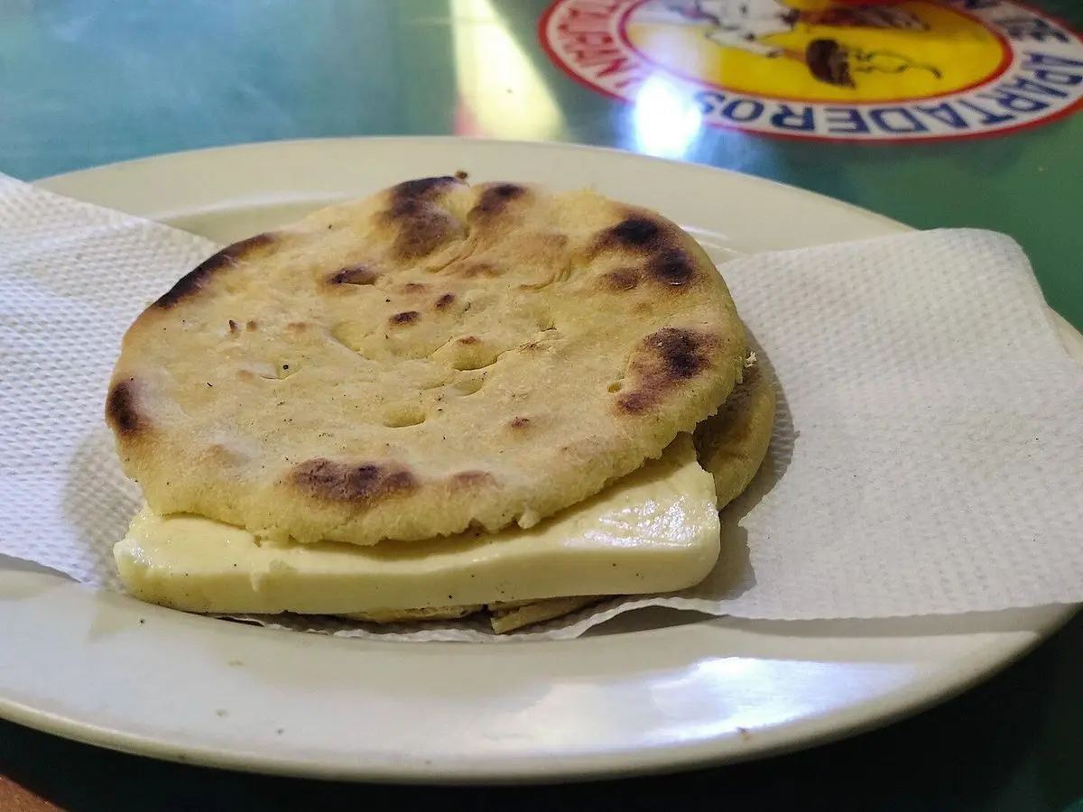 Arepa de trigo dorada sobre una loncha de queso blanco fresco en un plato con servilletas