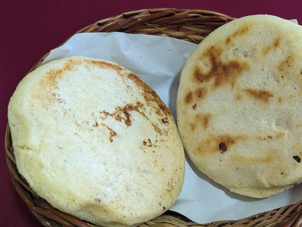 Arepas de maíz doradas en una cesta de mimbre con un paño blanco
