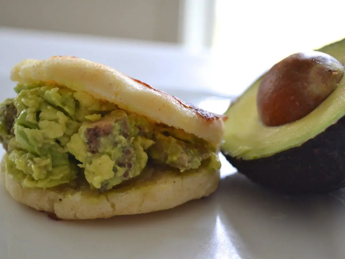 Arepa rellena de pollo y aguacate machacado junto a medio aguacate