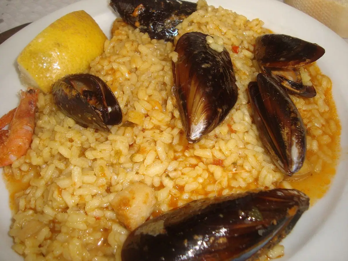 Plato de arroz meloso amarillo con mejillones abiertos y medio limón