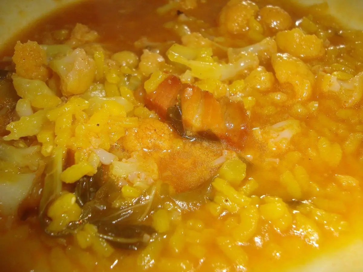 Plato de arroz caldoso dorado con trozos de costilla de cerdo y coliflor
