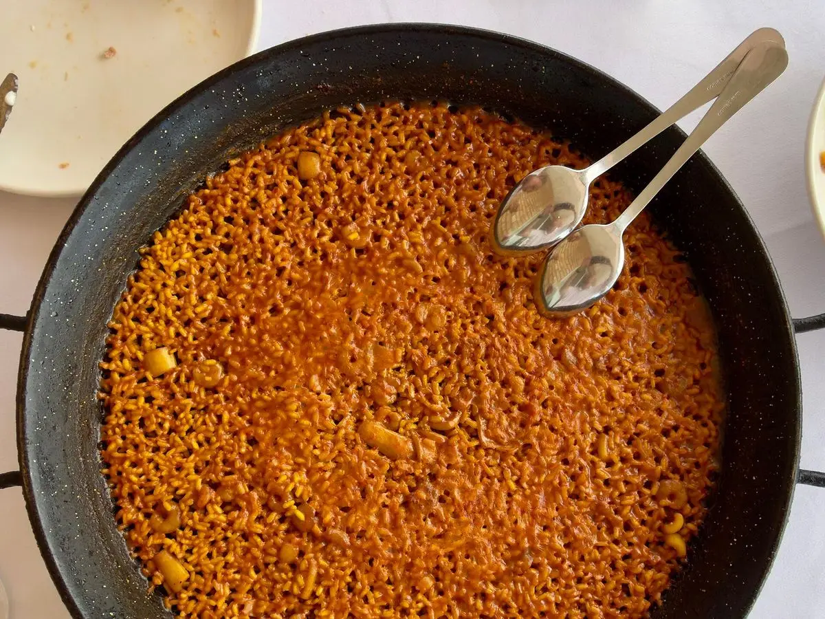 Arroz a banda dorado en una paella con pescado, servido en la mesa de un restaurante