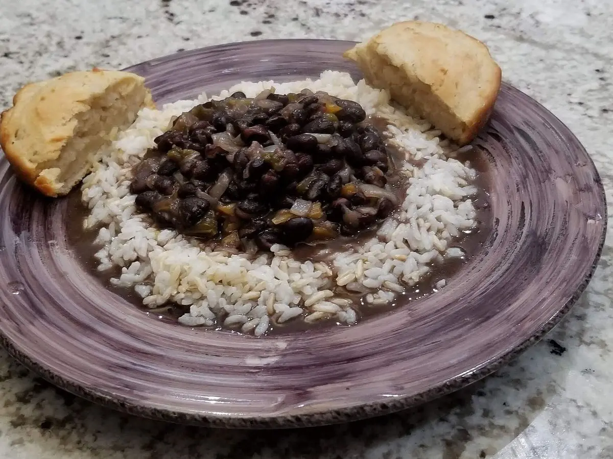 Plato de arroz blanco con alubias negras guisadas por encima y dos trozos de pan