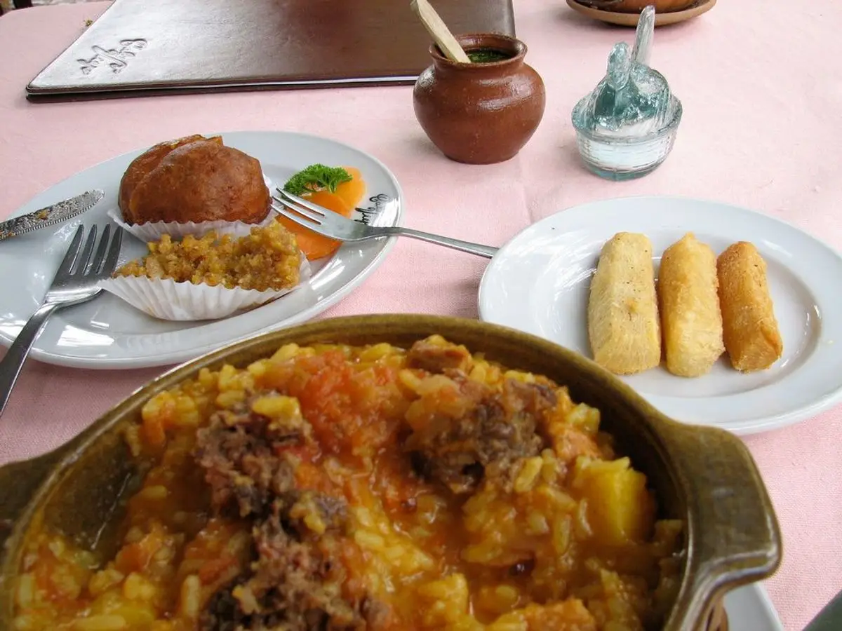 Cazuela de arroz caldoso amarillo con trozos de carne y patata junto a plátano frito