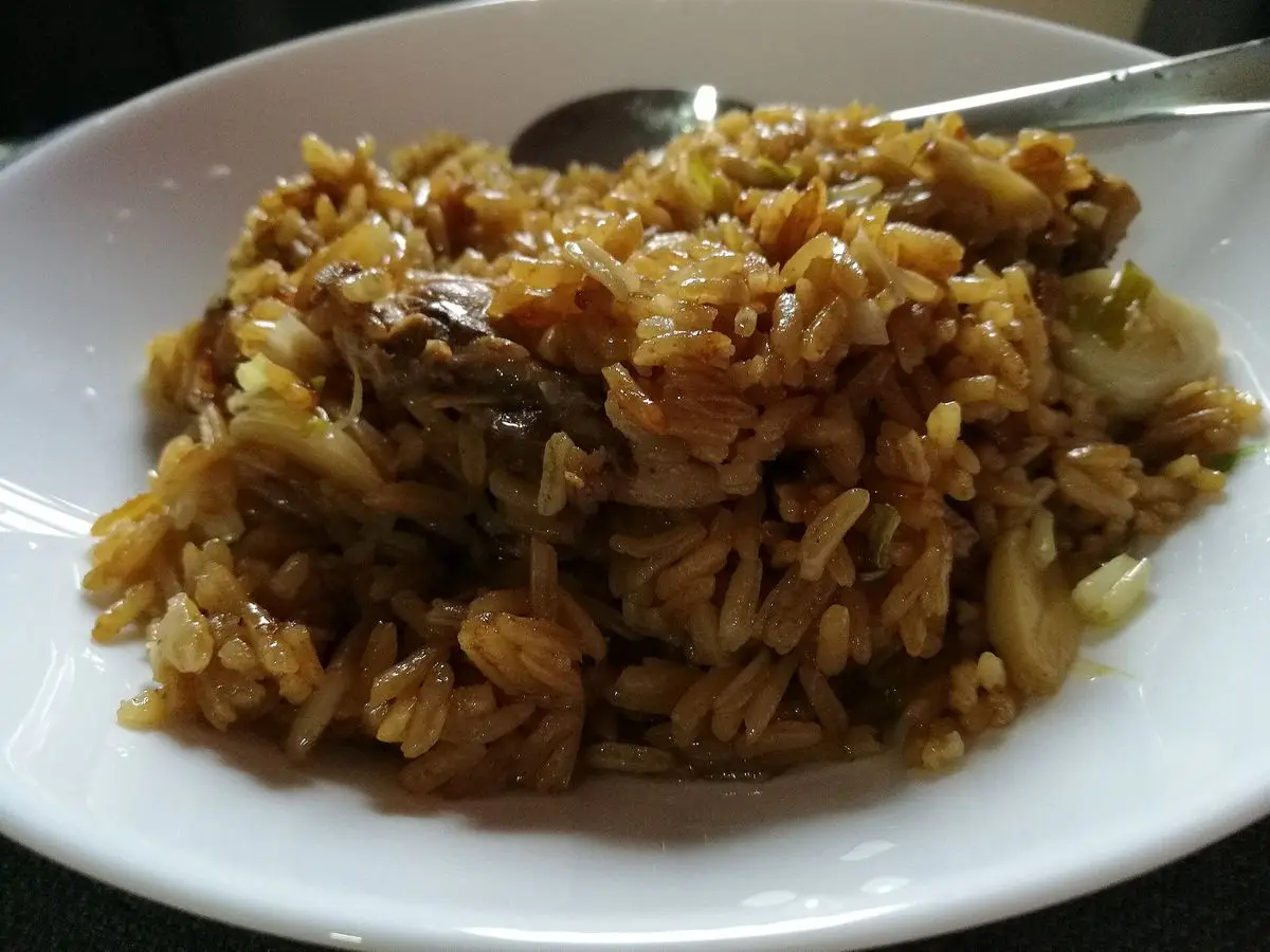 Plato blanco con arroz meloso oscuro con pollo y setas