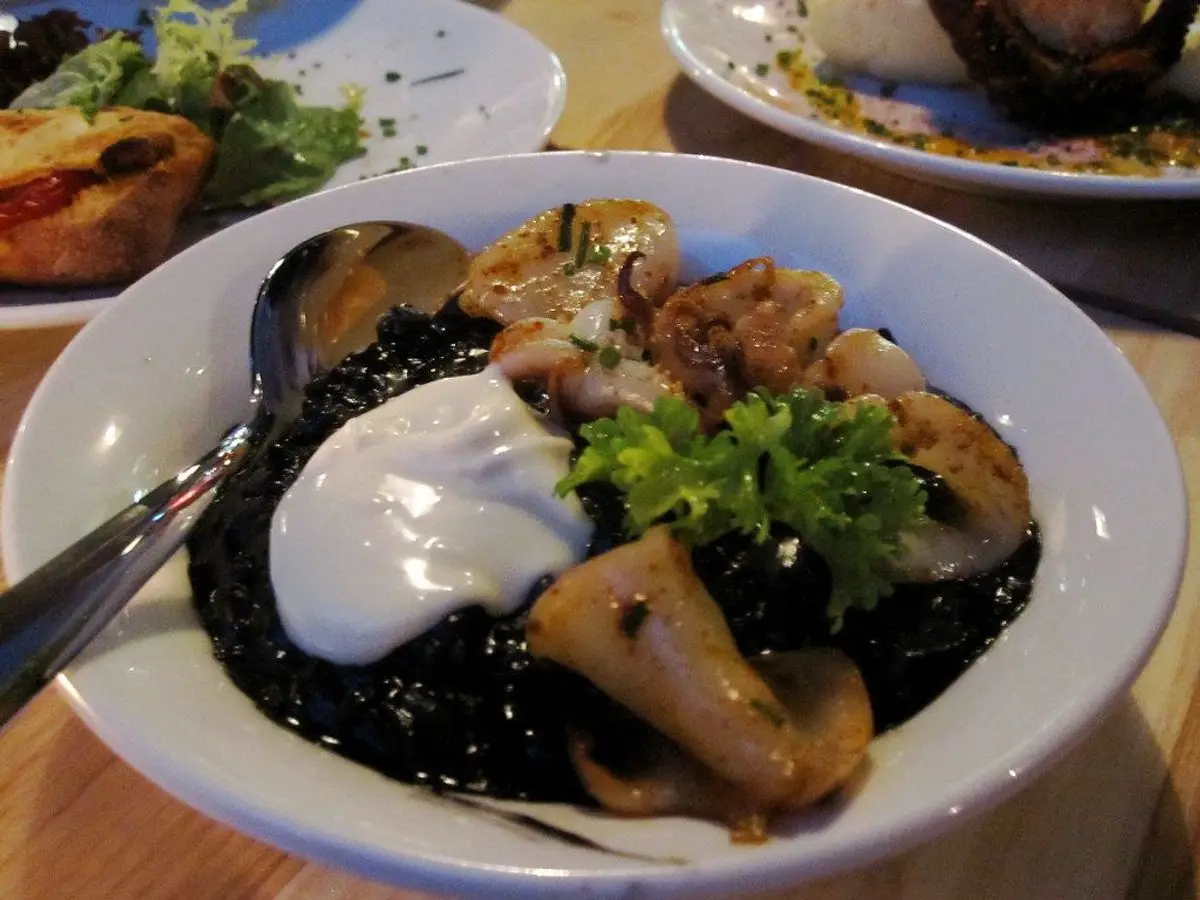 Arroz negro con calamar y setas, con alioli y perejil, en un cuenco blanco