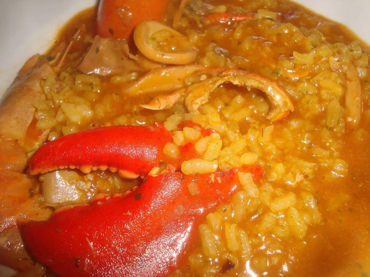 Arroz caldoso amarillo con pinza roja de bogavante y trozos de calamar en un plato