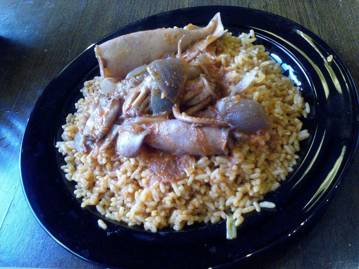 Arroz con calamares enteros pequeños sobre un plato negro hondo