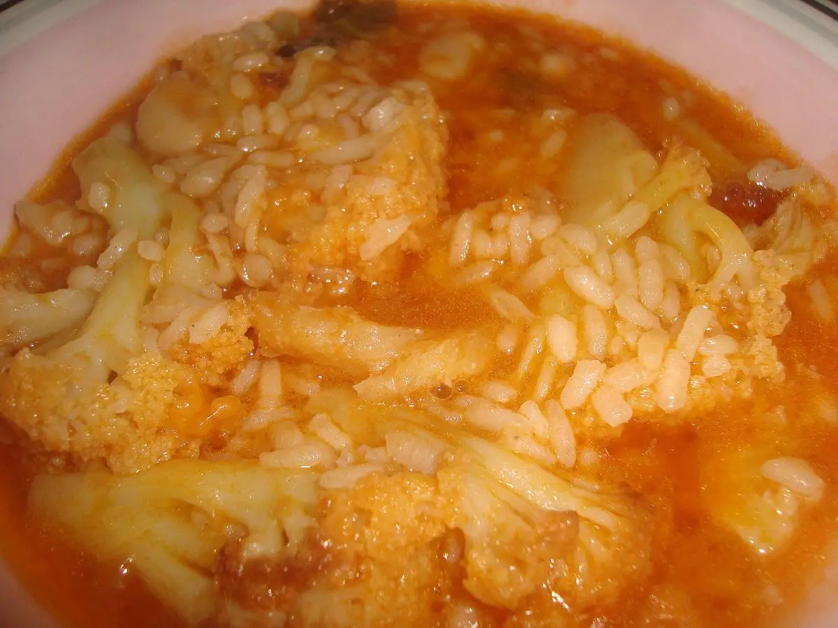 Plato hondo de arroz caldoso con trozos de coliflor en un caldo anaranjado