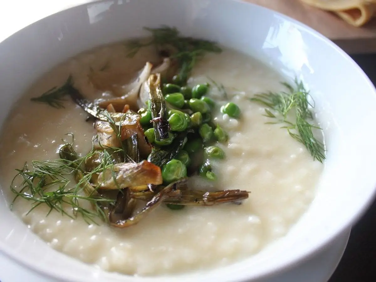 Plato hondo de arroz caldoso blanco con guisantes, eneldo y trocitos de carne por encima