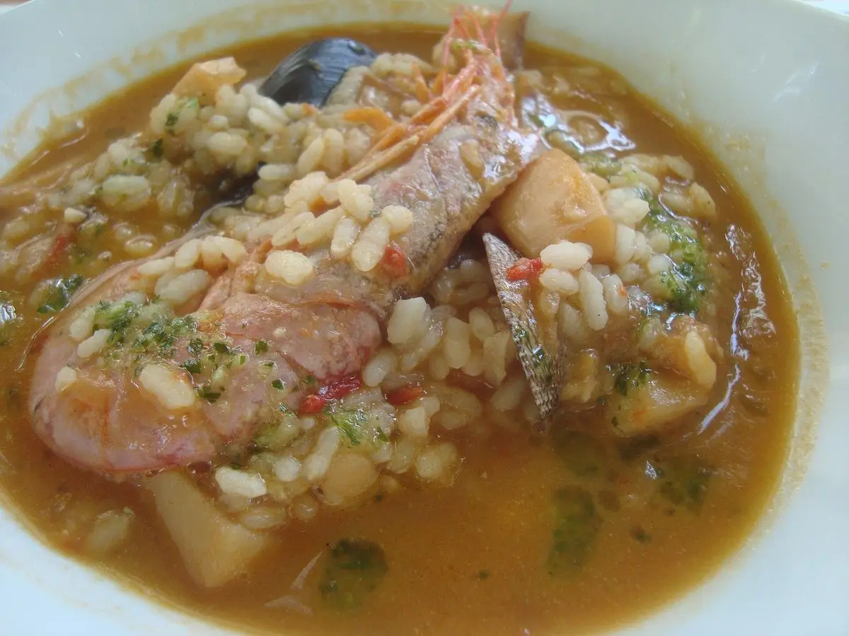 Plato hondo de arroz caldoso con gamba grande, pescado y perejil picado en caldo