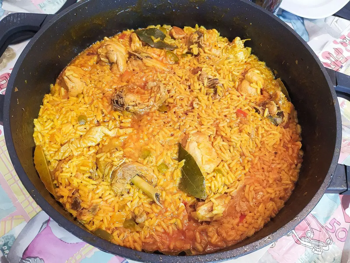 Cazuela negra de arroz anaranjado con trozos de pollo y verduras