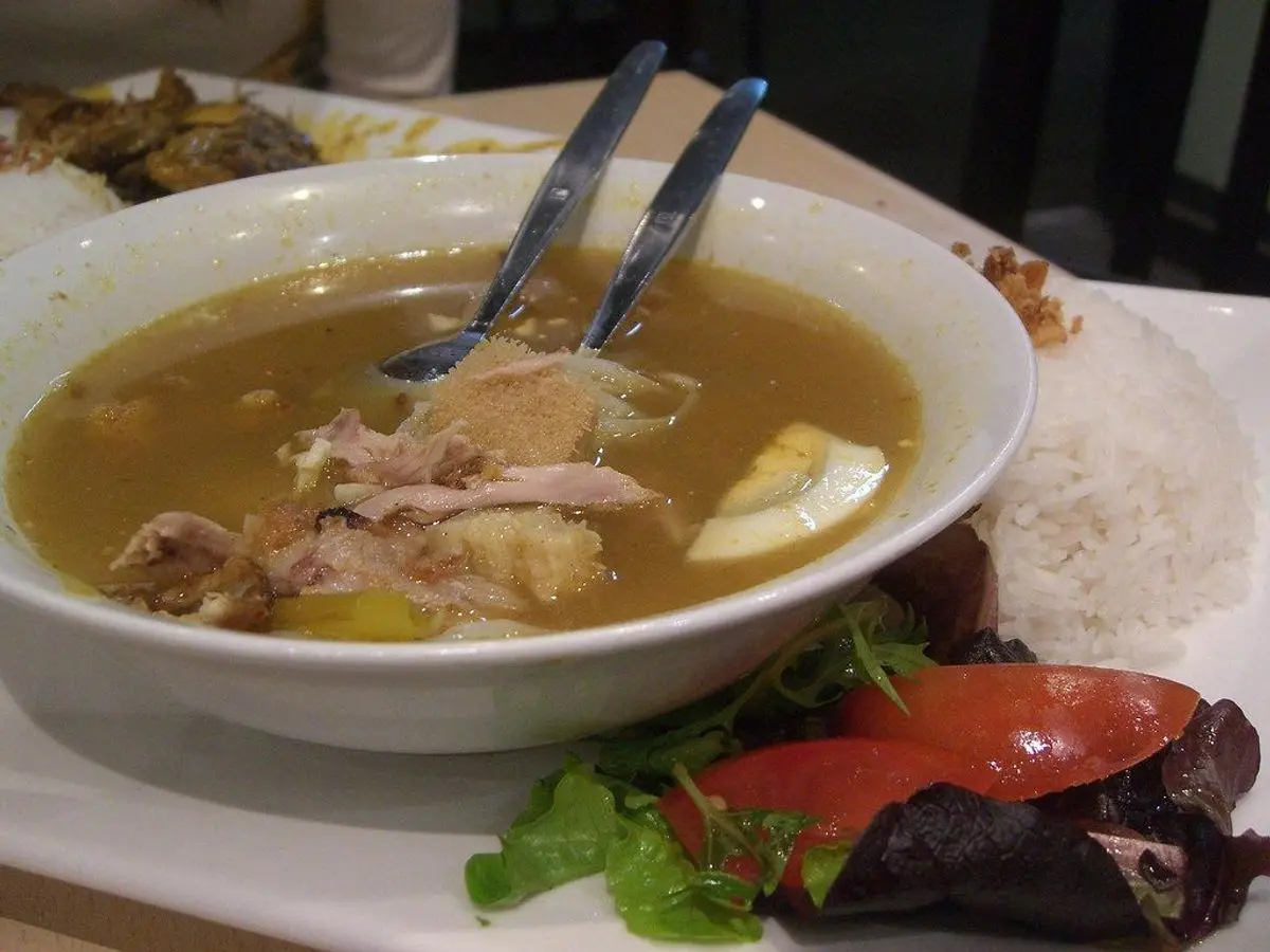 Cuenco de sopa con pollo y arroz, con rodajas de tomate y guarnición al lado