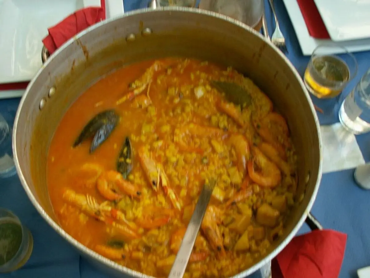 Olla grande de arroz caldoso anaranjado con mejillón y trozos de marisco