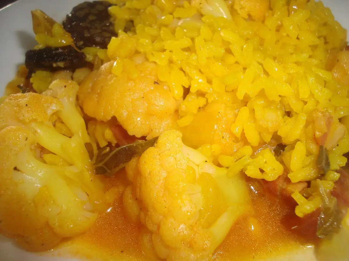 Plato de arroz caldoso amarillo con trozos de coliflor y verduras en un plato blanco