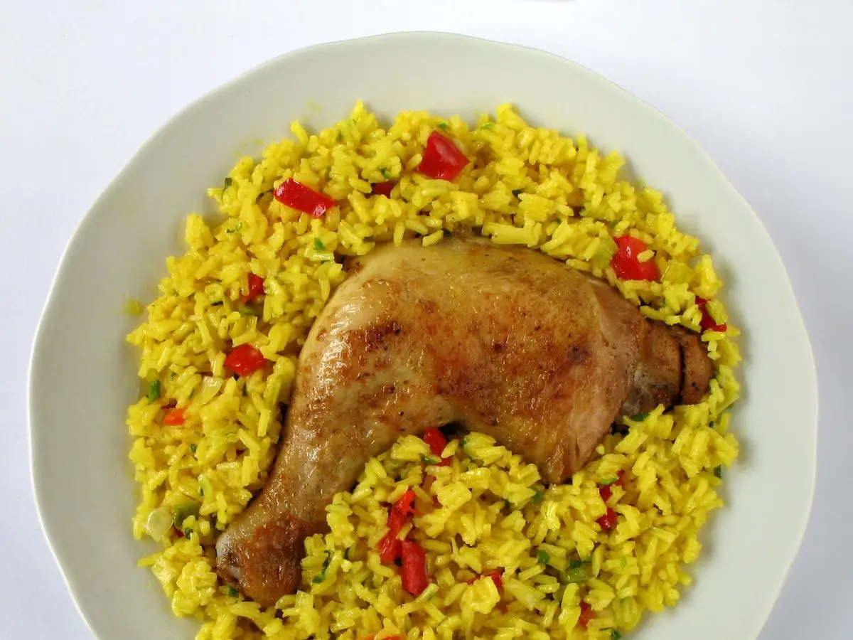 Plato blanco de arroz amarillo con pimiento rojo y un muslo de ave asado encima