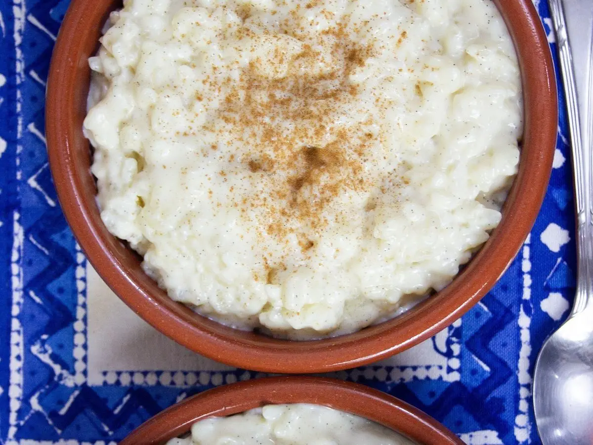 Cuenco de barro con arroz con leche cremoso espolvoreado de canela, sobre un mantel azul
