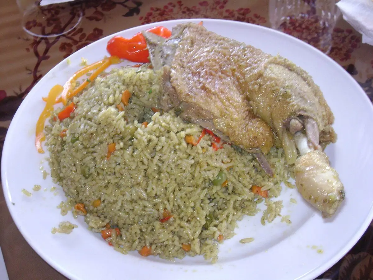 Arroz verde con cilantro y muslo de pato, con tomate y cebolla en un plato blanco