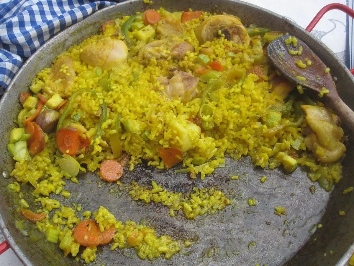 Paellera con arroz amarillo y trozos de pollo con verduras y una cuchara de servir