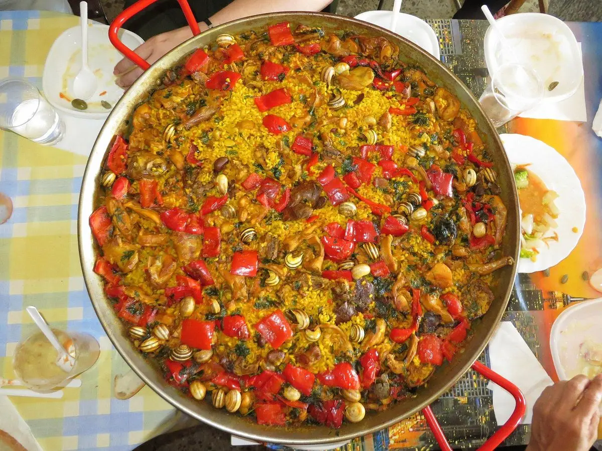 Paella de arroz con conejo, caracoles y pimiento rojo servida en la mesa