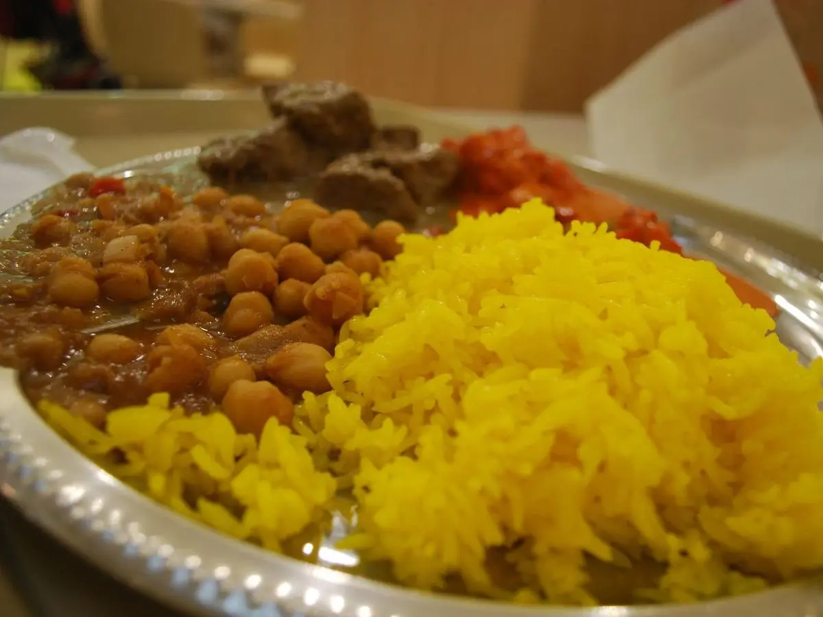 Bandeja metálica con arroz amarillo, garbanzos guisados y trozos de cordero