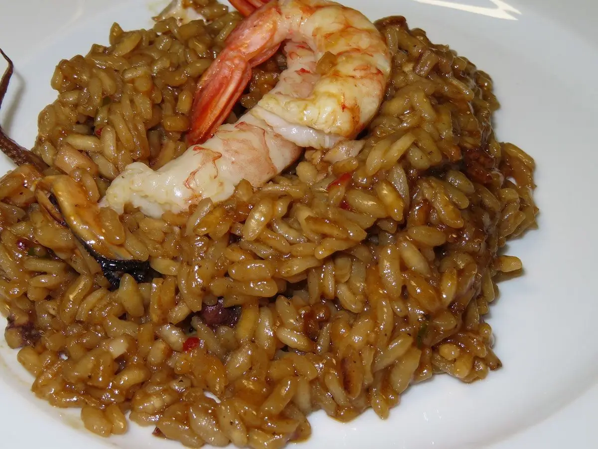 Arroz meloso con marisco y una gamba entera sobre el arroz en un plato blanco