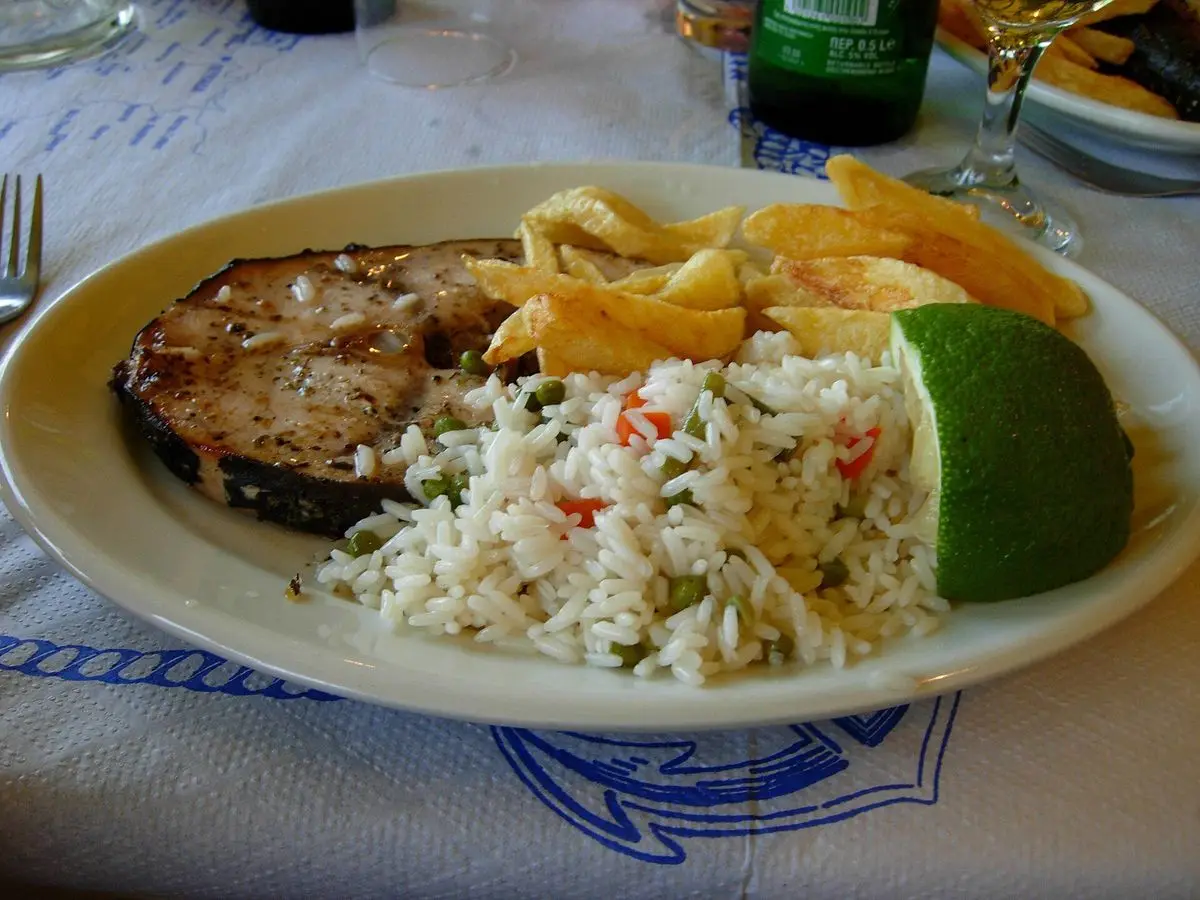 Plato con filete de pez espada a la plancha acompañado de arroz con verduras y una cuña de lima