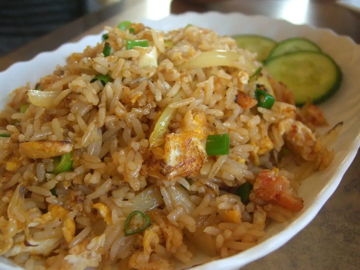 Arroz frito tailandés con carne de cangrejo y huevo, acompañado de rodajas de pepino en un plato blanco ovalado