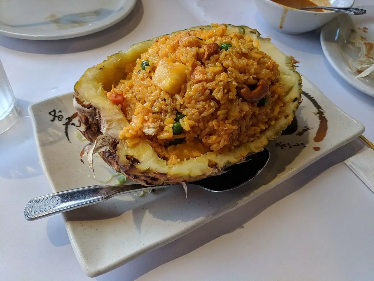 Arroz frito con trozos de piña servido dentro de una piña partida en un plato