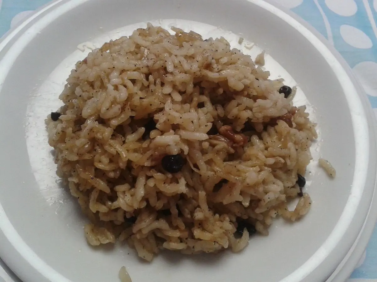 Plato blanco con arroz especiado y dorado, salpicado de pasas pequeñas y piñones