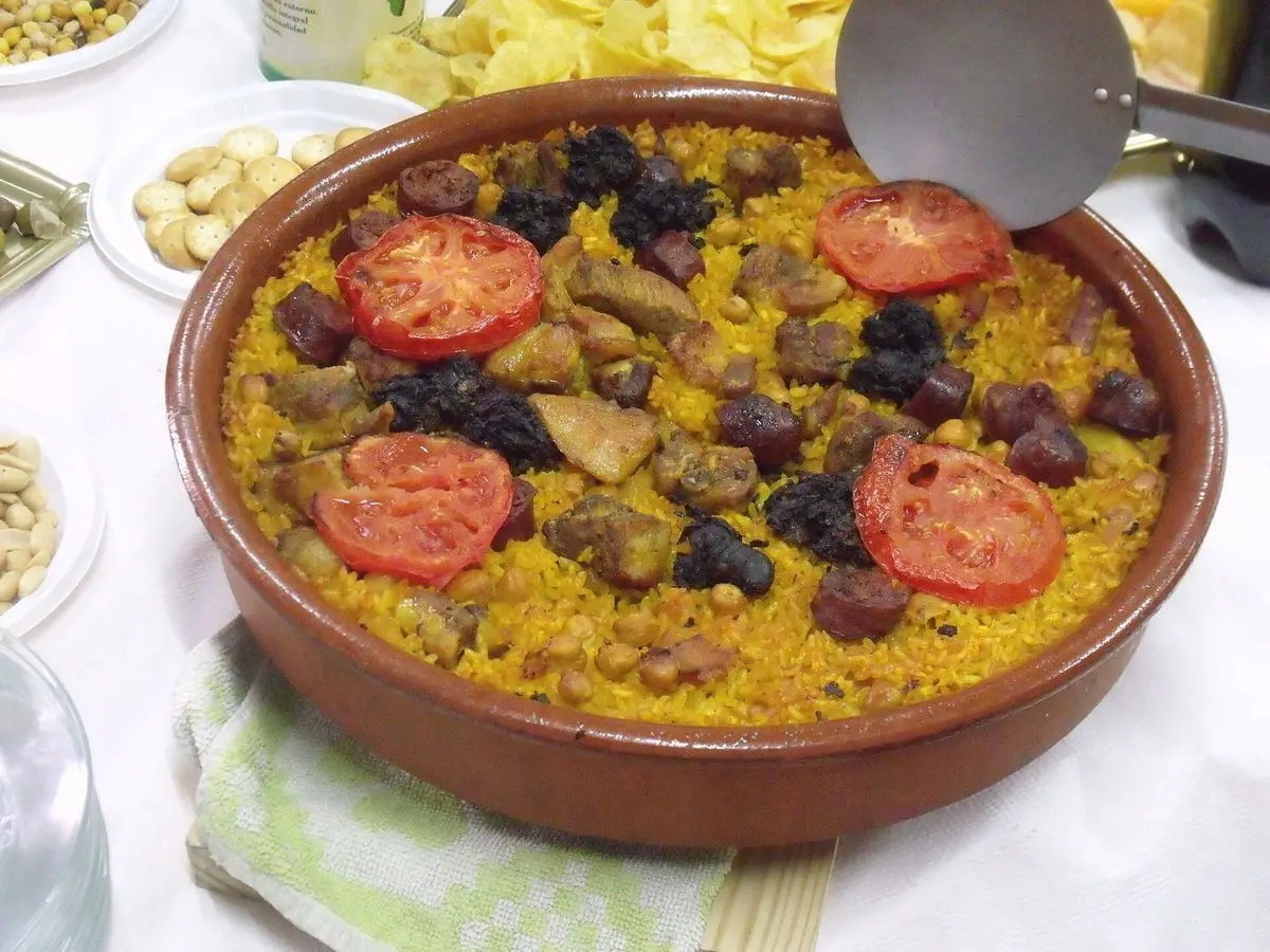 Cazuela de barro con arroz al horno, rodajas de tomate y trozos de carne