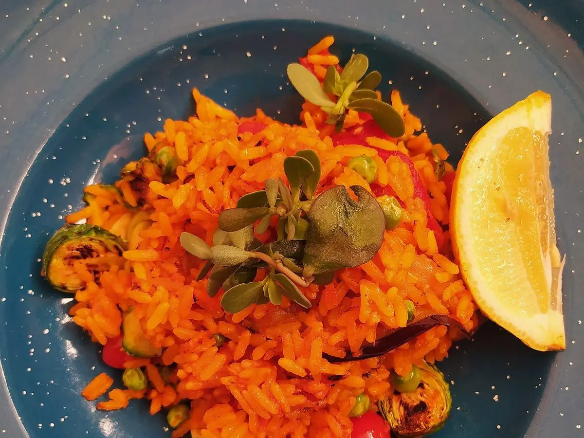 Plato azul con arroz anaranjado y verduras, tomate cherry y una rodaja de limón