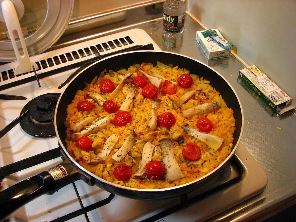 Sartén de arroz amarillo con tiras de pimiento rojo sobre los fogones de una cocina