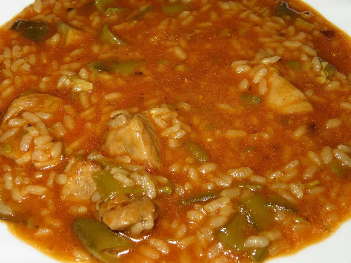 Arroz caldoso rojizo con trozos de pollo, alcachofas y pimiento en un plato