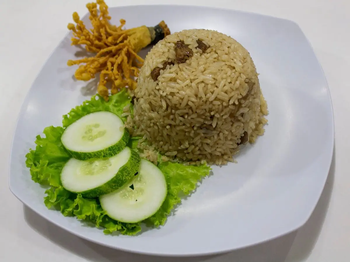 Montículo de arroz salteado con champiñones junto a rodajas de pepino, lechuga y fideos crujientes en un plato blanco