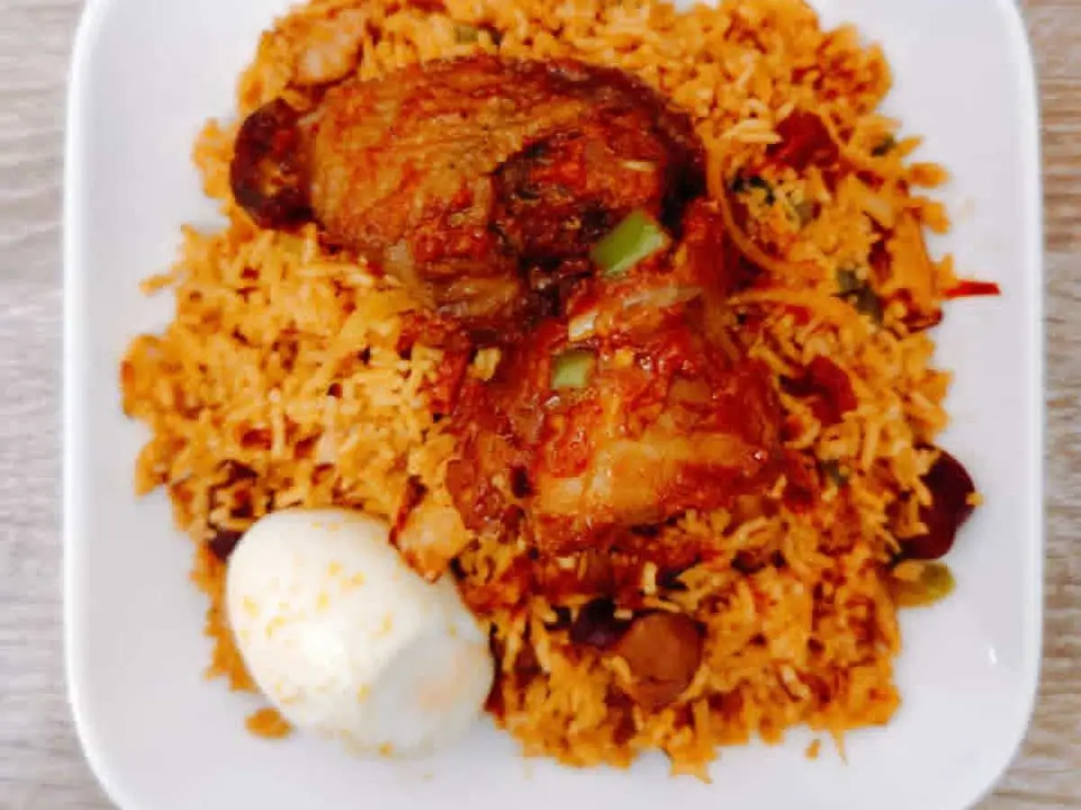 Arroz jollof anaranjado con muslo de pollo frito y huevo cocido en un plato blanco