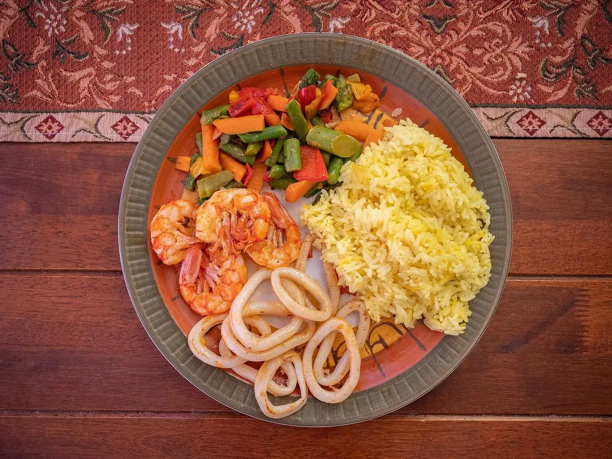 Plato con arroz amarillo, anillas de calamar, langostinos y verduras sobre una mesa de madera