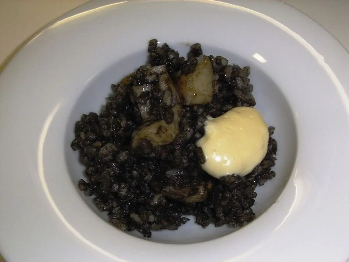 Plato hondo de arroz negro meloso con calamar y una cucharada de alioli