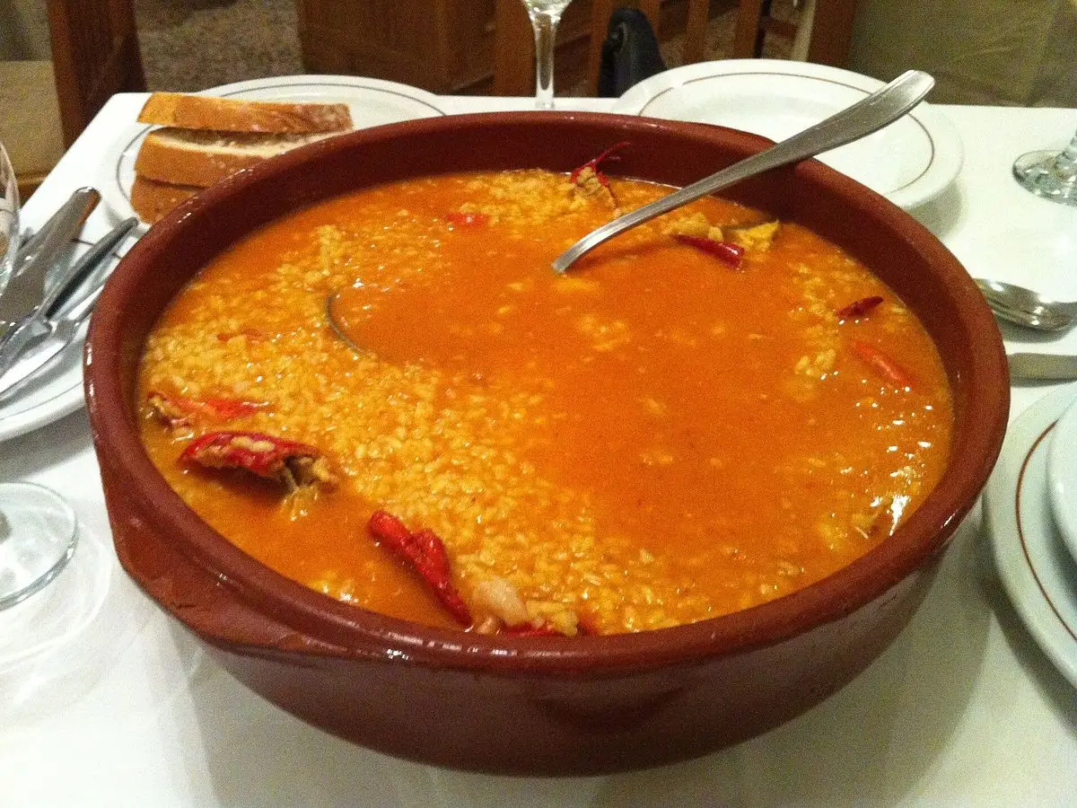Cazuela de barro con arroz meloso anaranjado y una cuchara metálica sobre una mesa