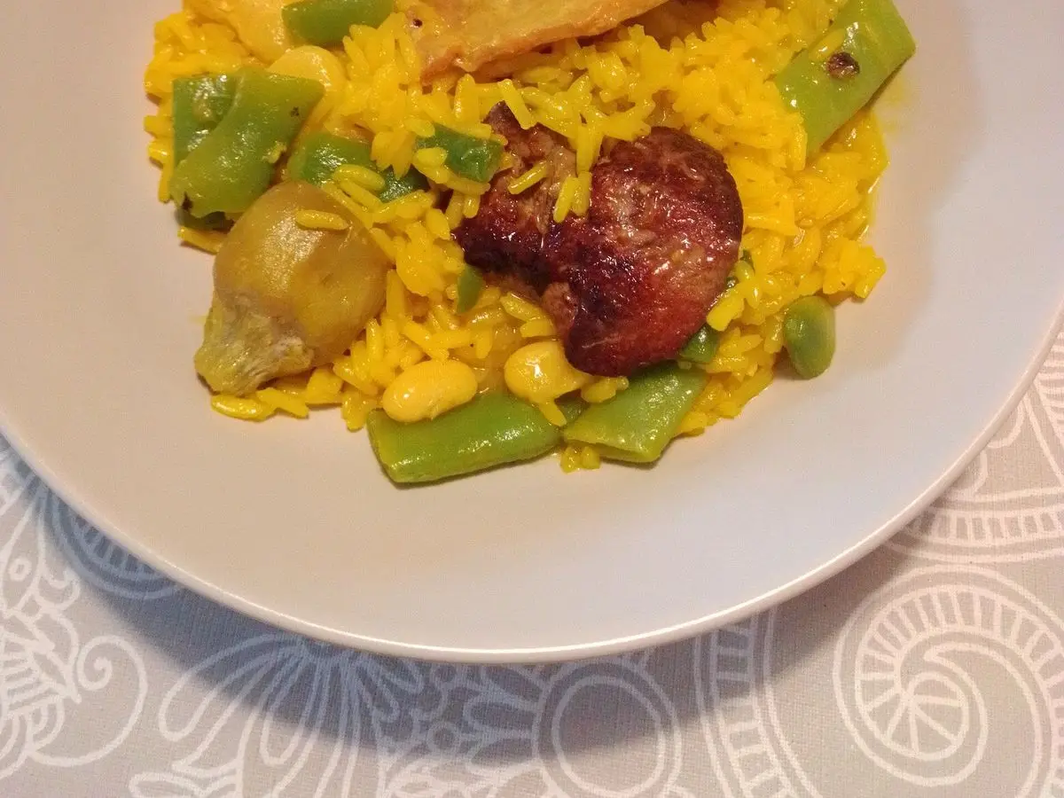 Plato de arroz amarillo con trozos de conejo, judía verde y alcachofa