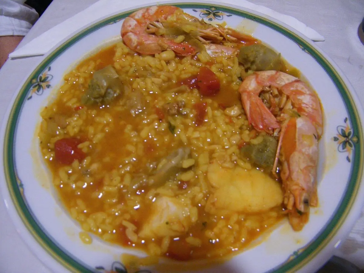 Plato hondo de arroz meloso con gambas enteras, alcachofa y patata sobre un mantel blanco