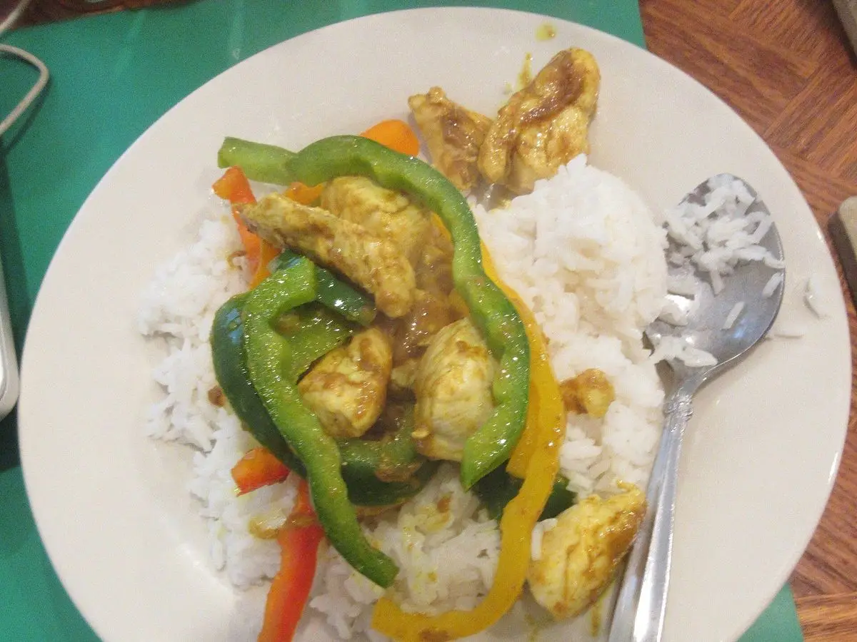 Plato de arroz blanco con pollo al curry, tiras de pimiento verde y amarillo y zanahoria