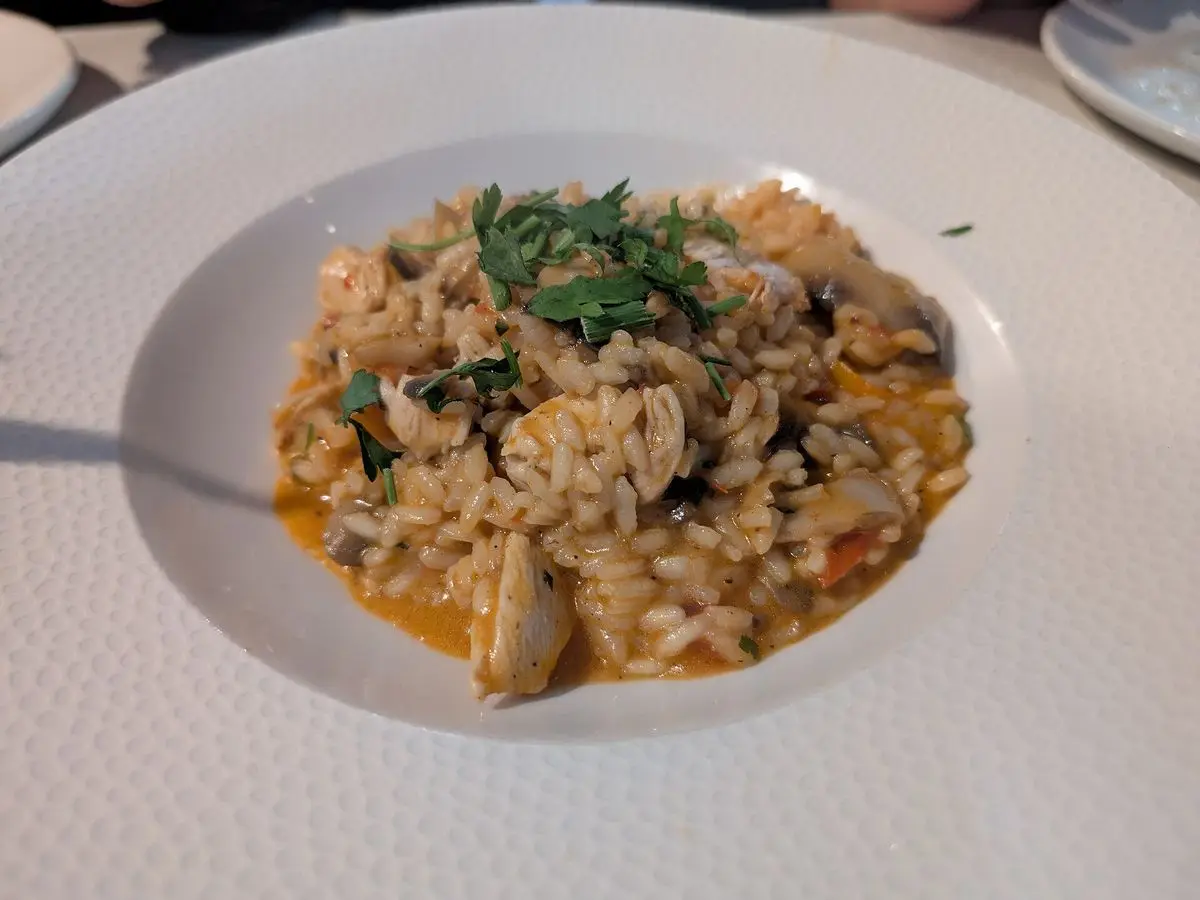 Plato hondo blanco con arroz cremoso con pollo, setas y perejil